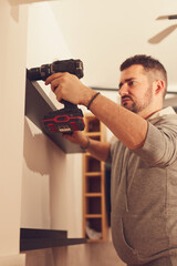 Wall Mural - Handyman with battery drill fixing kitchen cabinets and shelf.