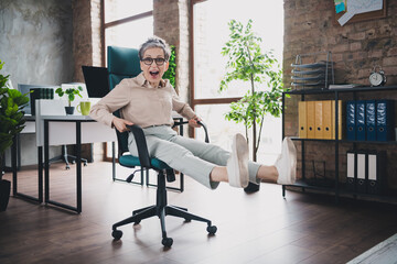 Poster - Photo of happy charming senior lady assistant wear formal shirt riding chair indoors workshop workstation loft