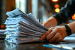 © Sergio - A close-up image of person sorting through large stack of papers on desk in modern office setting. The persons hand visible they carefully sift through documents, likely organizing or reviewing them