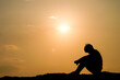 © STOCK PHOTO 4 U - Silhouette of a Person Sitting Alone at Sunset with a Golden Sky Background
