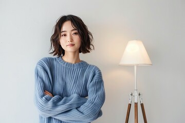 A woman in blue sweater standing with arms crossed in front of lamp