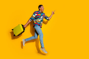 Full body photo of attractive young man suitcase run point empty space dressed stylish colorful clothes isolated on yellow color background