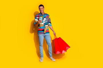 Full body photo of attractive young man hold device shopping bags dressed stylish colorful clothes isolated on yellow color background