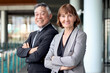 © Stella - Happy smiling senior Caucasian businesswoman in suit with Asian businessman standing with arms crossed at office. Elderly successful male and female boss at workplace. Portrait mature businesspeople.