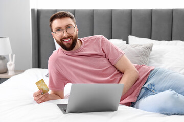 Canvas Print - Online banking. Happy young man with credit card and laptop paying purchase at home