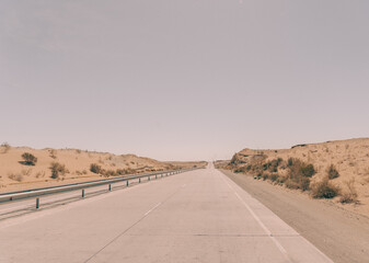 A road with no cars on it. The sky is clear and the sun is shining. The road is empty and there is no traffic