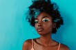 © pundapanda - A beautiful Afro young lady with vibrant blue hair and a pink top poses confidently against a plain turquoise background. Her striking features and bold colors create a stunning, eye-catching portrait