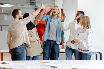 Diverse multinational team giving high five celebrating success in modern office