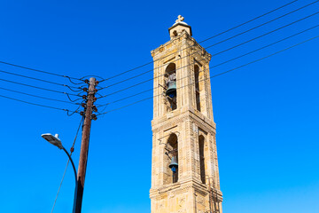 Wall Mural - Tall tower with a bell on top stands in front of a street light. Tower is surrounded by power lines, and the sky is clear and blue. Muslim belfry against sky