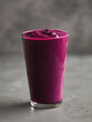 © SashaMagic - A tall glass filled with a vibrant purple smoothie on a gray background.