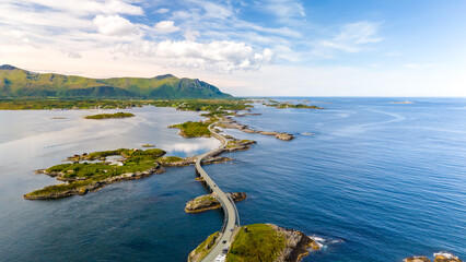 Wall Mural - A picturesque aerial view of the Atlantic Road in Norway, showcasing a winding bridge connecting small islands amidst stunning blue waters and a backdrop of rolling hills.