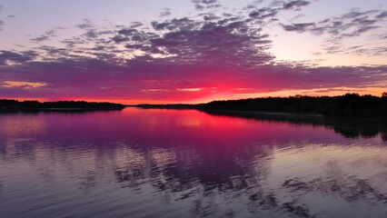 Wall Mural - Speed boat blasts through tranquil waters reflecting red dawn sky at sunrise.
