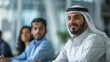 © Intelligent Horizons - Arab businessman in formal attire presenting a business plan or strategy to his colleagues in a corporate office setting using a projector screen  The team is gathered around a conference table