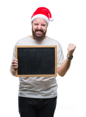 Sticker - Young caucasian hipster man wearing christmas hat holding blackboard over isolated background screaming proud and celebrating victory and success very excited, cheering emotion