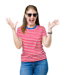 Wall Mural - Middle age mature woman wearing sunglasses over isolated background celebrating crazy and amazed for success with arms raised and open eyes screaming excited. Winner concept