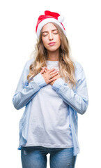 Wall Mural - Beautiful young blonde woman wearing christmas hat over isolated background smiling with hands on chest with closed eyes and grateful gesture on face. Health concept.