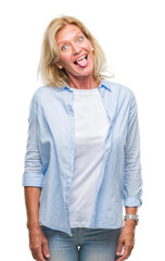 Wall Mural - Middle age blonde woman over isolated background sticking tongue out happy with funny expression. Emotion concept.