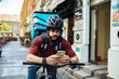 © Davor - Delivery man checking smartphone while standing with bicycle on city street