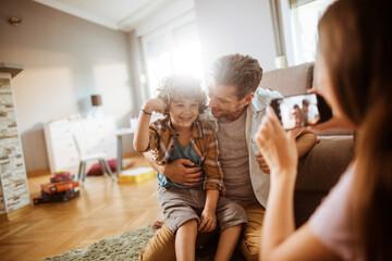 Wall Mural - Mother photographing father and son smiling together at home