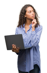 young hispanic woman holding computer laptop serious face thinking about question, very confused ide