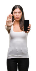 Sticker - Young beautiful hispanic showing smartphone with open hand doing stop sign with serious and confident expression, defense gesture