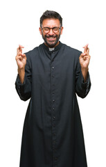 Poster - Adult hispanic catholic priest man over isolated background smiling crossing fingers with hope and eyes closed. Luck and superstitious concept.