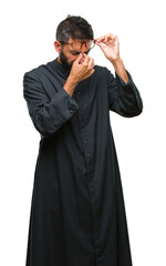 Canvas Print - Adult hispanic catholic priest man over isolated background tired rubbing nose and eyes feeling fatigue and headache. Stress and frustration concept.