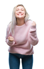 Sticker - Young blonde woman wearing winter sweater over isolated background very happy and excited doing winner gesture with arms raised, smiling and screaming for success. Celebration concept.