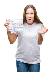 Sticker - Young caucasian woman holding menstruation calendar over isolated background scared in shock with a surprise face, afraid and excited with fear expression