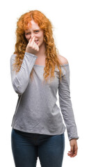 Canvas Print - Young redhead woman smelling something stinky and disgusting, intolerable smell, holding breath with fingers on nose. Bad smells concept.