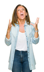 Wall Mural - Middle age adult woman wearing casual denim shirt over isolated background crazy and mad shouting and yelling with aggressive expression and arms raised. Frustration concept.