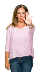 Wall Mural - Beautiful middle age adult woman wearing winter sweater over isolated background doing stop sing with palm of the hand. Warning expression with negative and serious gesture on the face.