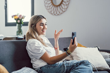 Happy cheerful beautiful 20s woman resting on home couch, typing on mobile phone, using online app, software, shopping on Internet, talking on video call. Smartphone communication.