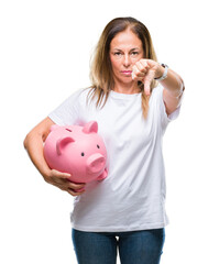 Poster - Middle age hispanic woman saving money using piggy bank over isolated background with angry face, negative sign showing dislike with thumbs down, rejection concept