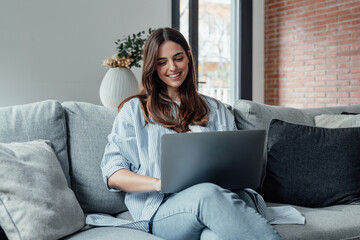 concentrated millennial girl sit on couch working on laptop browsing internet at home during lazy we