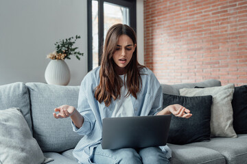 Wall Mural - Angry young woman sit on sofa in living room frustrated having operational problems working on laptop, mad millennial girl feel stressed confused with slow internet connection or computer spam.