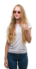 Wall Mural - Blonde teenager woman wearing sunglasses happy with big smile doing ok sign, thumb up with fingers, excellent sign