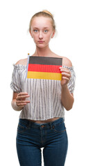 Sticker - Blonde teenager woman holding flag of Germany with a confident expression on smart face thinking serious