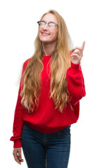 Sticker - Blonde teenager woman wearing red sweater showing and pointing up with finger number one while smiling confident and happy.