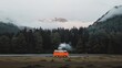 © Dumrongkait - A red van is parked in a field next to a forest. The van is the only vehicle in the scene