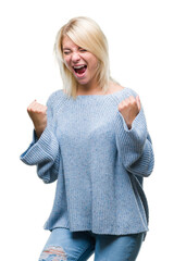 Wall Mural - Young beautiful blonde woman wearing winter sweater over isolated background very happy and excited doing winner gesture with arms raised, smiling and screaming for success. Celebration concept.