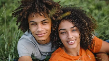 Wall Mural - A young man and woman are sitting in the grass, smiling at the camera