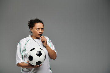 Wall Mural - A female referee blows her whistle while holding a soccer ball.