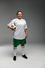 Wall Mural - Female athlete in white jersey and green shorts, prepared for action with soccer ball.