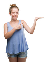 Wall Mural - Young blonde woman amazed and smiling to the camera while presenting with hand and pointing with finger.