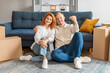 © Home-stock - Happy young family couple showing keys from new own home, sitting on floor carpet near carton boxes. Real estate concept