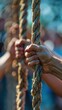 © Naret - Close-up of hands gripping thick ropes during a team-building outdoor activity or competition, emphasizing teamwork and strength.