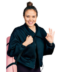 Wall Mural - Young hispanic girl holding yoga mat doing ok sign with fingers, smiling friendly gesturing excellent symbol