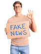 © Krakenimages.com - Young handsome man holding fake news banner doing ok sign with fingers, smiling friendly gesturing excellent symbol