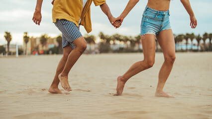 Wall Mural - A young couple of Hispanic descent enjoys a leisurely walk along the shoreline, dressed casually for the beach, with entwined hands suggesting affection.